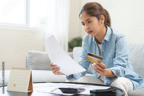 Business financial concept, stressed asian young business woman holding credit card and bill for calculate accounting expense of bill, tax for payment on due deadline, trying to find money to pay debt