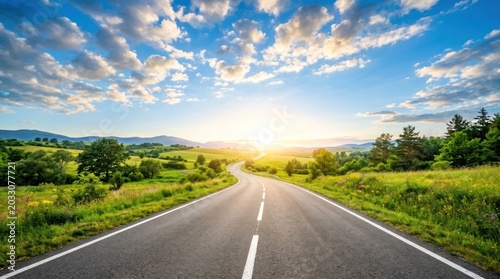 A sunny road stretches into the distance, winding through a lush green valley. The road is asphalt, with white lane markings.