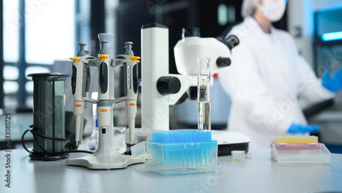 Scientific Laboratory Workbench with Micropipettes, Microscope, and Test Equipment with Researcher in Background