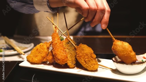 居酒屋で串カツにたっぷりとソースをつける若い女性の手元（クローズアップ）