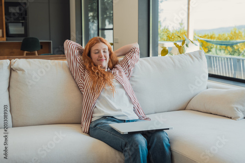 Obraz na płótnie Young adult woman with red hair closing eyes and stretching while sitting on a c