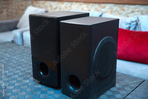 interior, providing high quality loud audio sound and home theater entertainment . Modern black LG stereo speakers with a subwoofer subsystem are placed on a textured dark table in a cozy living room
