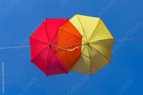 two colourful umbrellas, one red and one yellow, hanging from a rope against the backdrop of a blue sky on a sunny day