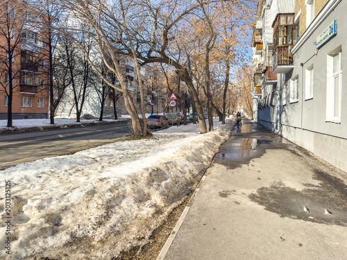 Fényképezés Snowy sidewalk alongside residential buildings in urban spring setting
