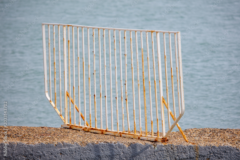Fototapeta premium Weathered metal barrier rests on rocky shoreline