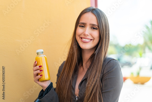 Фотография Young woman holding an orange juice at outdoors smiling a lot