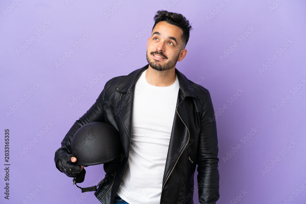 Fototapeta premium Young man with a motorcycle helmet isolated on purple background thinking an idea while looking up