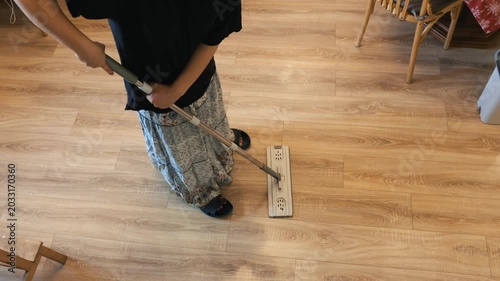 A teenager uses a flat mop on a light wooden floor during everyday household chores indoors.
