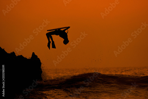 Photography Dramatic silhouette of an extreme athlete performing a high-flying backflip on a bodyboard against a vibrant orange and golden sunset sky