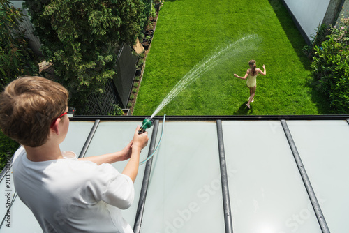 Happy children are playing with water in the garden this summer. A family is playing with a garden hose at home—full of fun and high spirits.