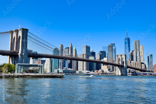 Brooklyn Bridge and Lower Manhattan skyline viewed from East River with boat and One World Trade Center on sunny day, New York City, USA
