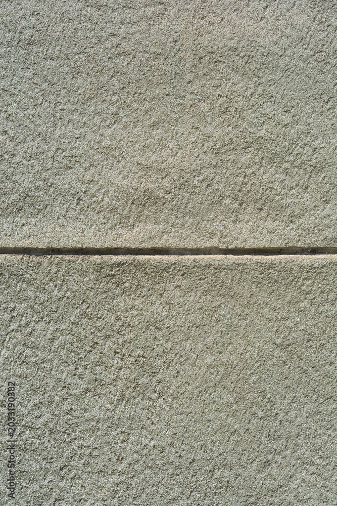 Fototapeta premium A close up background texture of a rough grey plaster building wall divided by a deep horizontal groove