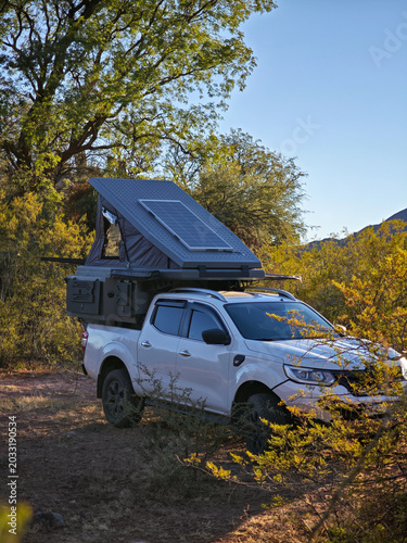 Overland 4x4 truck equipped with a rooftop tent and solar panel camping in nature.