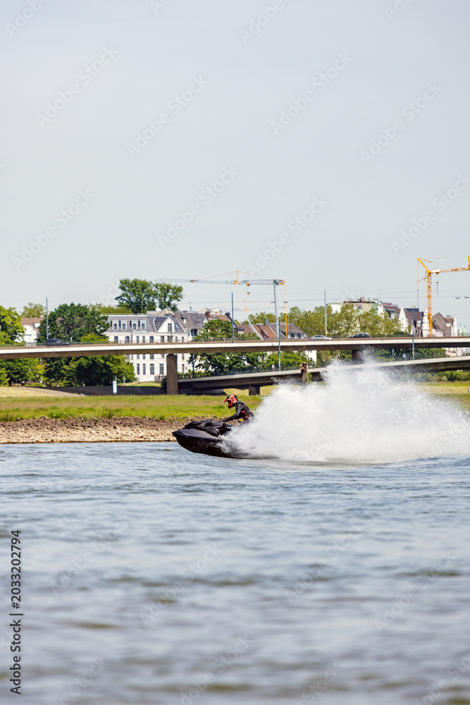 Fototapeta premium Rider Executing Swift Turns On Waterway. Watercraft Slicing Through River With Spray In Urban Setting