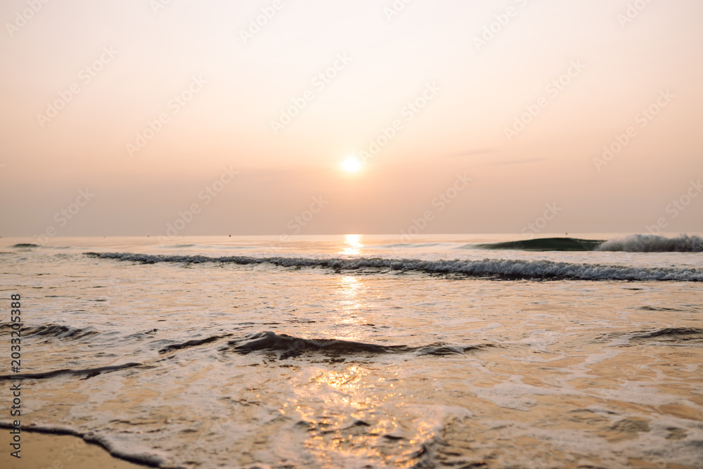 Obraz premium Sunset on the beach, gentle waves, and buildings in the distance along the coastline. Seascape. A tranquil landscape, sea waves at sunset. Concept of nature and beauty.