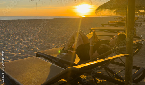 Beautiful middle-aged woman sitting on sandy beach on sunset on spring day. Back view. beach on Algarve coast in Portugal