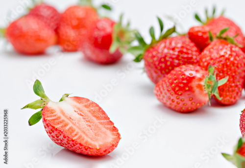 Close up of a fresh red strawberry half on white background with blurry whole strawberries in selective focus