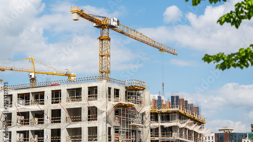 Schilderij op canvas Construction crane towers over unfinished concrete buildings