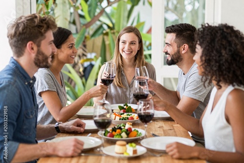 Diverse group of friends raising wine glasses together in a celebratory toast at a dinner party