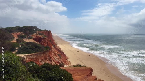 Landscape view of the Algarve coast, red cliffs, several pine trees on the upper part of the cliffs, beautiful blue sky