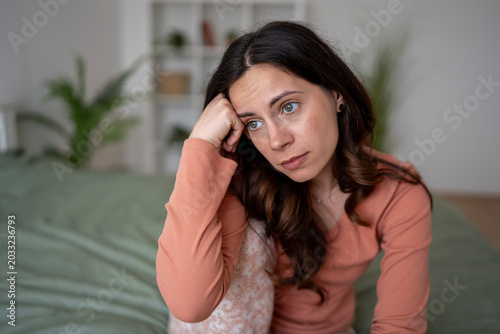 Young woman feeling sad and anxious sitting on bed