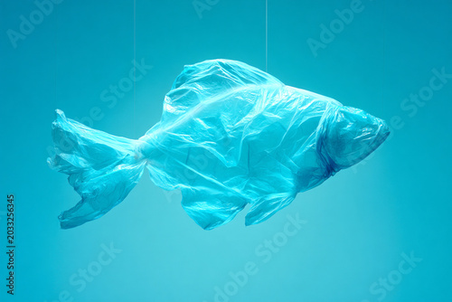 Plastic bag shaped like fish suspended in blue background to illustrate ocean pollution and environment crisis