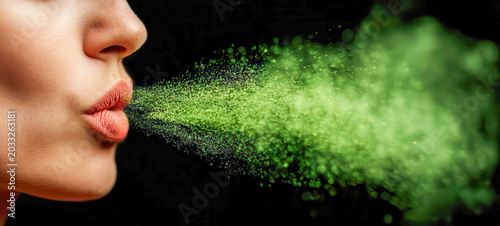 Woman blows green powder into the air against a black background during an artistic performance