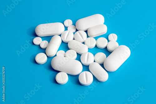 Many different white medicine tablets lie on a blue background.	