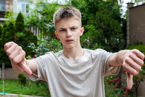 Canvas-taulu Unhappy teenage boy showing thumbs down gesture outdoors, disapproval and negati