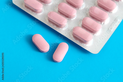 On a blue background lies a blister pack with medicine in pink capsules.
