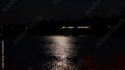 Glares of illumination light and moon on water surface and sky against night background. Web banner.