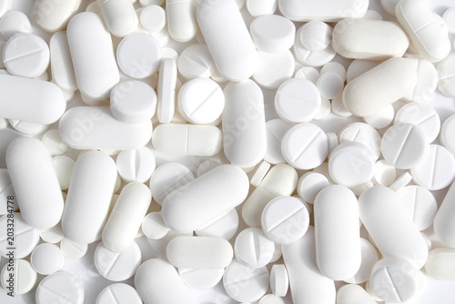 There are many different white pills lying on a white background.