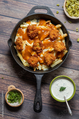 A skillet of deep fried pickle poutine with pickle toppings, ready for serving.