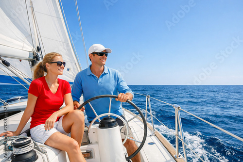 Happy adult couple in sunglasses sailing on a luxury yacht during a bright sunny day at sea