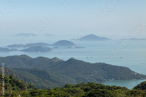 Panoramic view of islands and coastline near Hong Kong with hazy blue sea and lush green mountains in natural daylight.