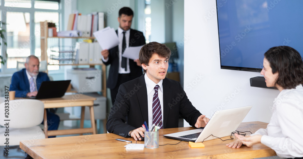 © JackF - Young male bank employee at desk with laptop and discussing with adult female customer