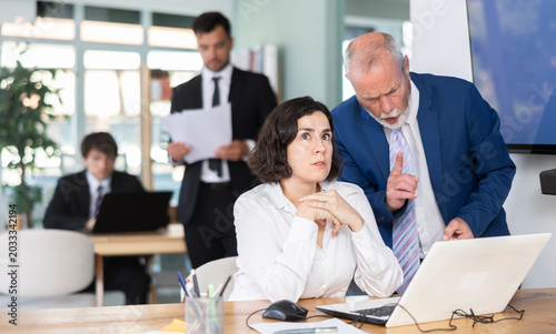 Tableau sur toile Strict mature man boss scolding girl office worker for improper operation on lap