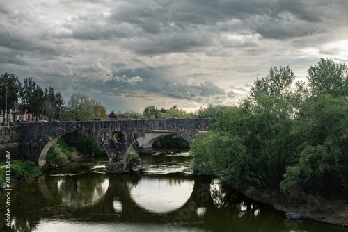 Roman stone bridge over the Volturno River in Capua with a cloudy sky. Ideal for tourism promotion, editorial content about the Caserta area, or conceptual design.