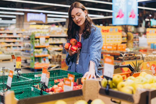 Fotografi Woman shopping for fresh red apples in supermarket produce section, choosing hea