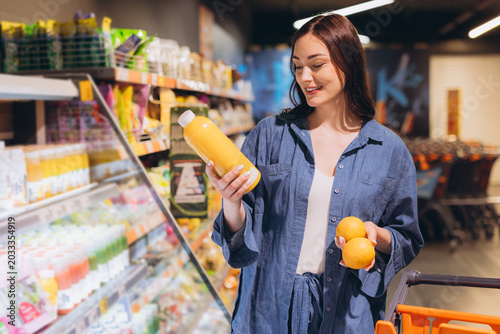 Photography Young woman evaluating orange juice product ingredients while comparing fresh fr