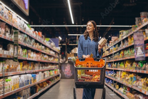 Tableau sur toile Young woman shopping for groceries in a supermarket aisle, choosing food product