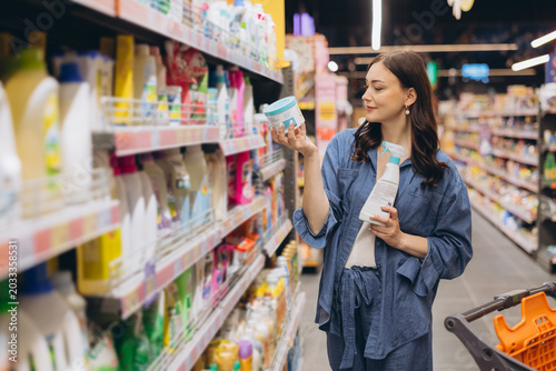 Fotografi Woman choosing cleaning supplies and looking at product packaging in supermarket