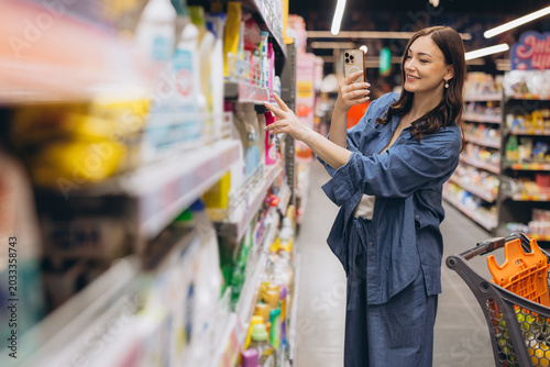 Tableau sur toile Woman shopping in grocery store, using smartphone to scan product information, c