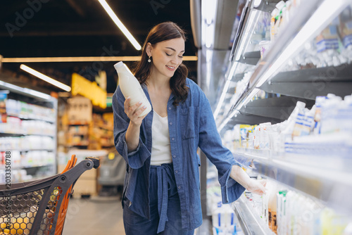 Canvastavla Woman buying dairy at supermarket, holding milk bottle and choosing product from