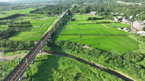 Aerial view of a high-speed bullet train crossing a river bridge amid green farmlands.