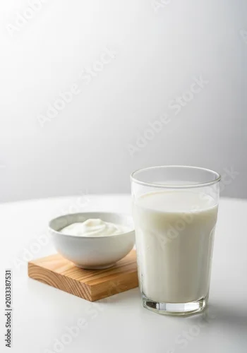 Fototapeta na wymiar A fresh glass of cold milk stands on a white table next to a wooden block and a small bowl of creamy yogurt in a clean, minimal setting, white, refreshment, dairy