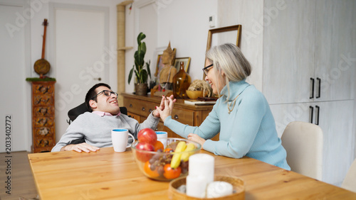 Man with a physical condition and his mother connecting at home, sharing smiles and a heartfelt moment