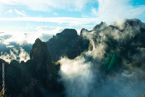 Foto Dramatic mountain crags and steep volcanic cliffs pierced by bright morning sunlight with rolling white clouds in the valley