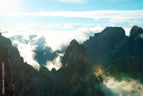 Billede på lærred Dramatic mountain crags and steep volcanic cliffs pierced by bright morning sunlight with rolling white clouds in the valley