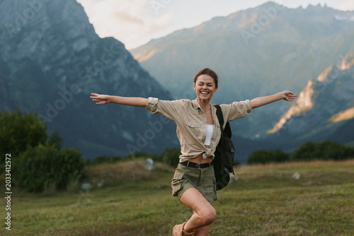 Obraz na płótnie Smiling woman outdoors in a mountainside field, arms spread, casual outfit